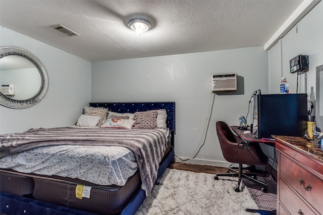 bedroom with wood-type flooring, a textured ceiling, and a wall unit AC