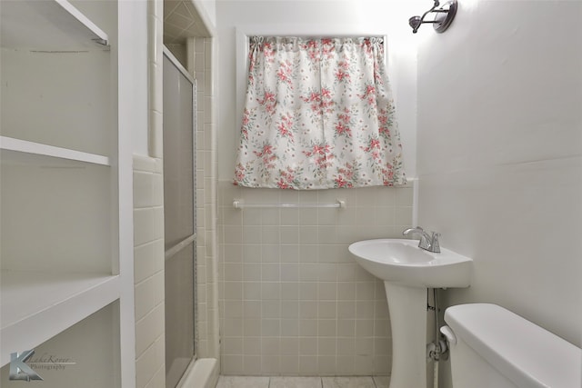 bathroom with sink, tile patterned floors, toilet, a shower with shower door, and tile walls