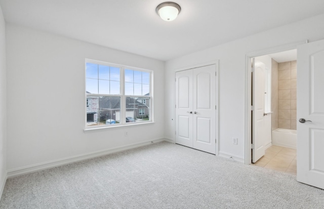 unfurnished bedroom featuring ensuite bath, a closet, and light colored carpet