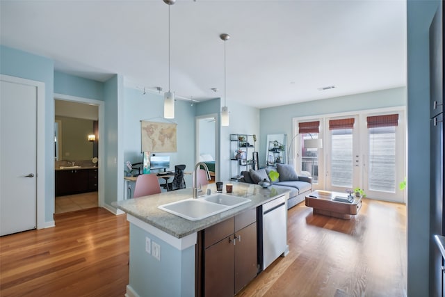 kitchen featuring sink, stainless steel dishwasher, hardwood / wood-style floors, decorative light fixtures, and a center island with sink