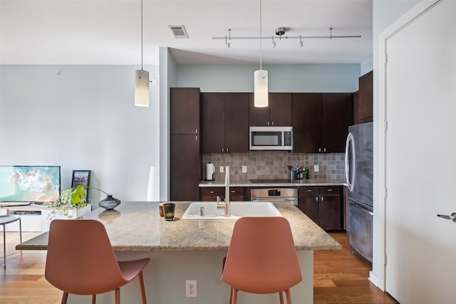 kitchen featuring hanging light fixtures, stainless steel appliances, light hardwood / wood-style flooring, a breakfast bar area, and dark brown cabinets