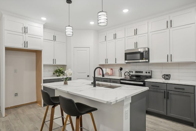 kitchen featuring appliances with stainless steel finishes, decorative light fixtures, a kitchen island with sink, white cabinetry, and a sink