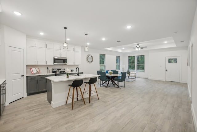 kitchen featuring ceiling fan, hanging light fixtures, stainless steel appliances, an island with sink, and white cabinets