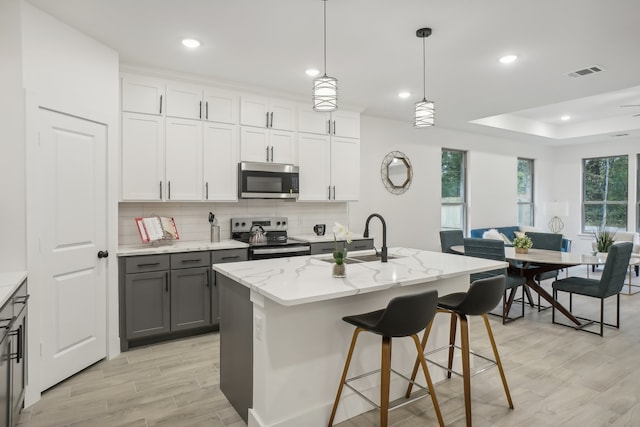 kitchen featuring appliances with stainless steel finishes, white cabinetry, a wealth of natural light, and an island with sink