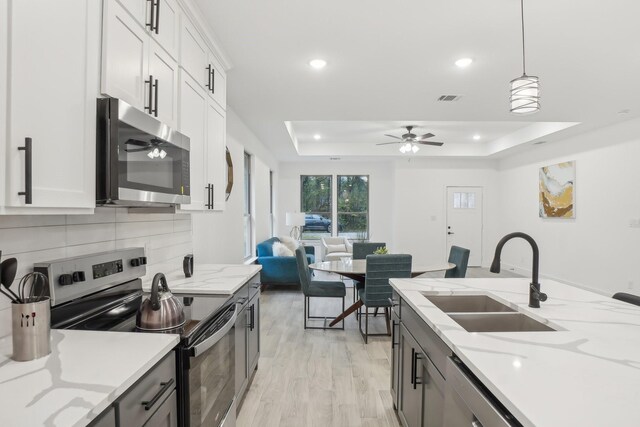 kitchen featuring sink, hanging light fixtures, stainless steel appliances, a tray ceiling, and white cabinets