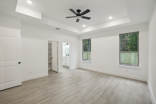 unfurnished bedroom featuring ensuite bathroom, ceiling fan, light wood-type flooring, and a spacious closet