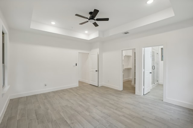 unfurnished bedroom featuring a raised ceiling, ceiling fan, light hardwood / wood-style flooring, a spacious closet, and a closet