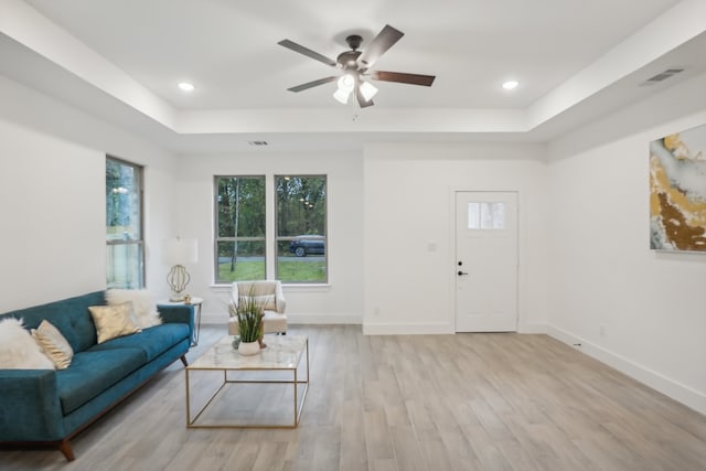 living room with ceiling fan, a tray ceiling, and light hardwood / wood-style flooring