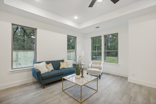 living room with a raised ceiling, ceiling fan, a healthy amount of sunlight, and light wood-type flooring