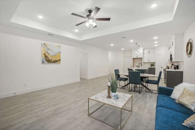 living room featuring a raised ceiling, light wood-type flooring, and sink