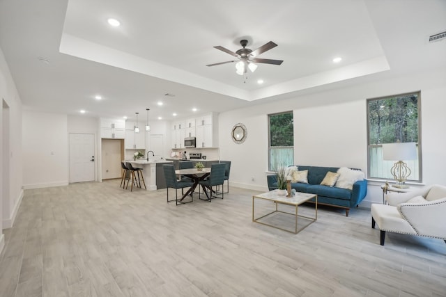 living area featuring a tray ceiling, baseboards, light wood finished floors, and recessed lighting