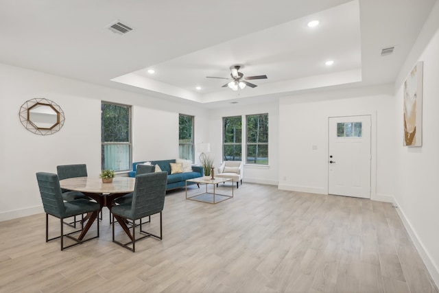 dining space with a tray ceiling, ceiling fan, and light wood-type flooring