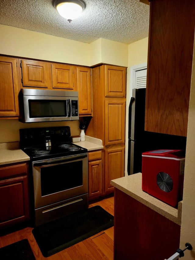 1200 Riverchase Ln Unit 226, Arlington, TX 76011 - kitchen featuring stainless steel appliances, brown cabinetry, a textured ceiling, light countertops, and wood finished floors