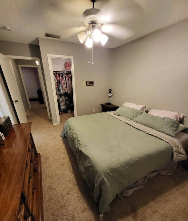 carpeted bedroom featuring a walk in closet, ceiling fan, a closet, and a textured ceiling