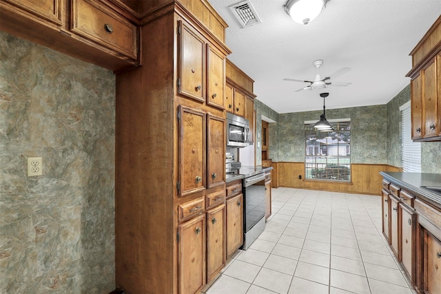 kitchen with ceiling fan, decorative light fixtures, wooden walls, light tile patterned floors, and appliances with stainless steel finishes