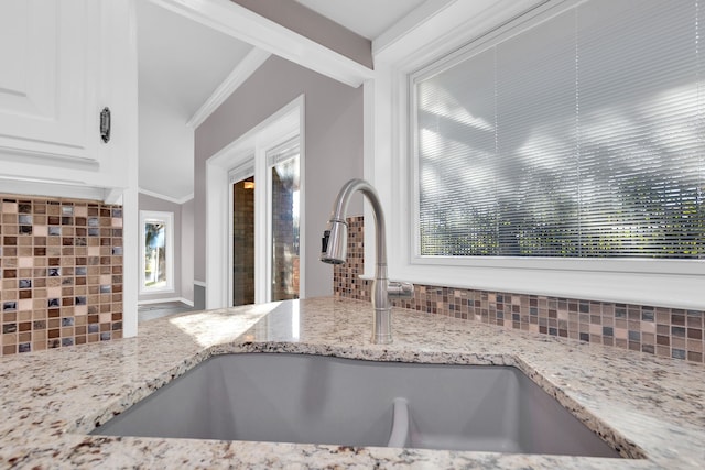 kitchen featuring backsplash, light stone counters, crown molding, sink, and white cabinets