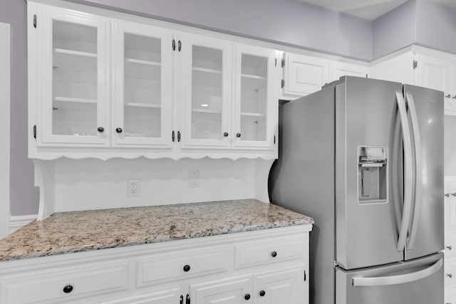 kitchen with light stone countertops, white cabinets, and stainless steel refrigerator with ice dispenser