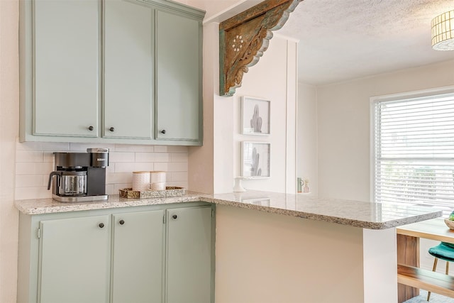 kitchen with kitchen peninsula, decorative backsplash, light stone counters, green cabinetry, and a textured ceiling