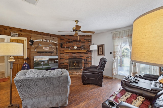 living room featuring wood walls, a brick fireplace, ceiling fan, a textured ceiling, and dark hardwood / wood-style flooring