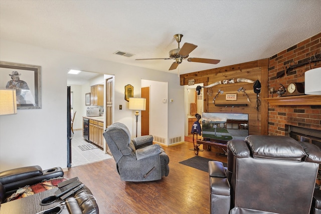 living room with ceiling fan, a fireplace, a textured ceiling, and light wood-type flooring