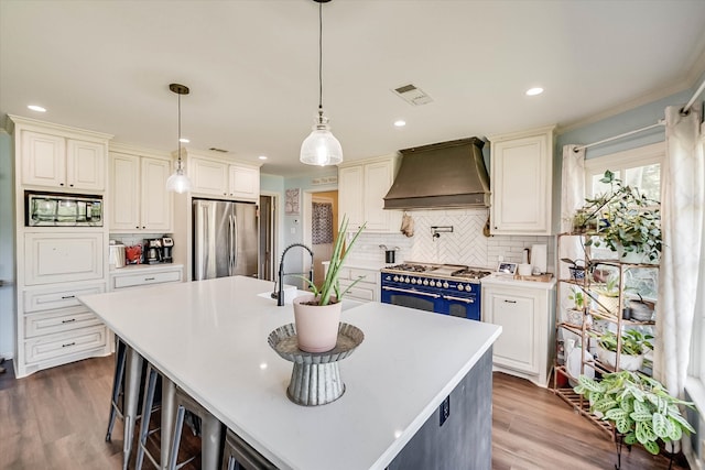 kitchen with a kitchen island with sink, light hardwood / wood-style flooring, stainless steel appliances, and custom range hood