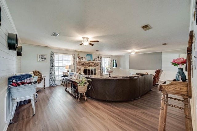 living room with a brick fireplace, hardwood / wood-style flooring, ceiling fan, ornamental molding, and a textured ceiling