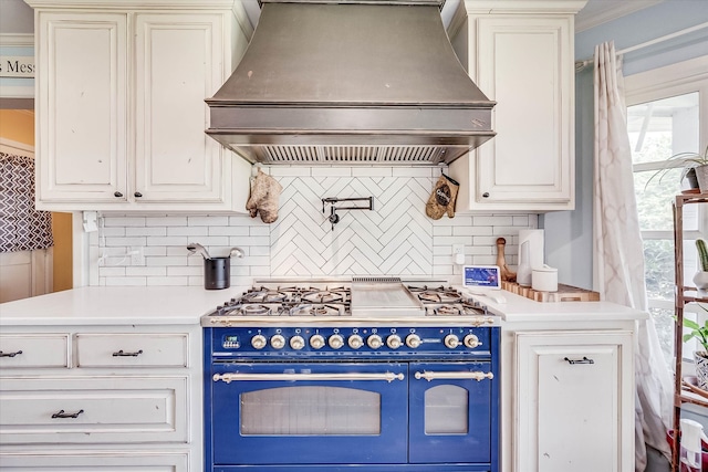 kitchen featuring gas range oven, custom range hood, decorative backsplash, and blue cabinetry