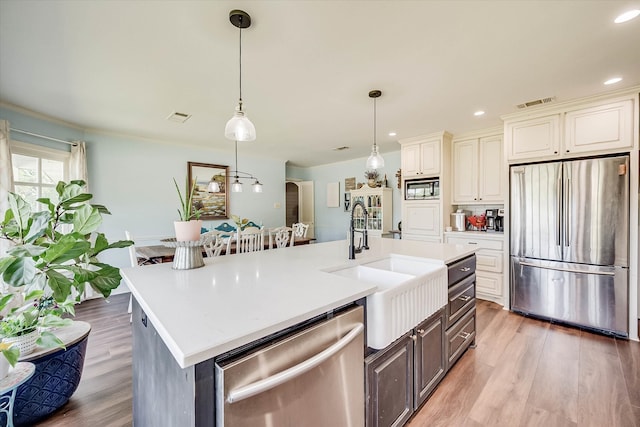 kitchen featuring dark wood-type flooring, hanging light fixtures, an island with sink, and stainless steel appliances