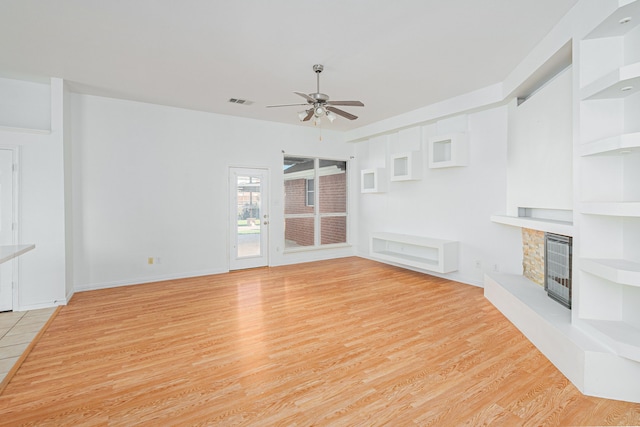 unfurnished living room featuring a stone fireplace, ceiling fan, and light hardwood / wood-style floors