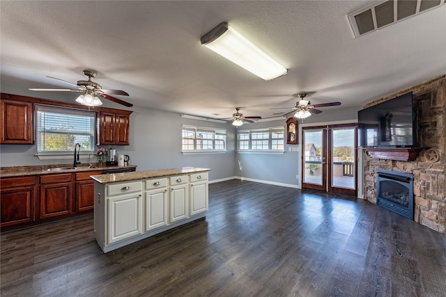 kitchen featuring a center island, a stone fireplace, dark wood-type flooring, and sink