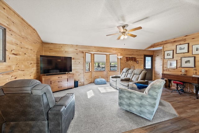 living room with lofted ceiling, wooden walls, hardwood / wood-style flooring, ceiling fan, and a textured ceiling