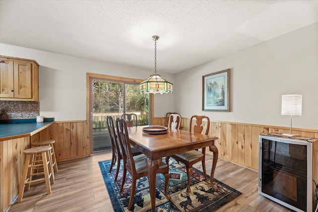 dining area with wine cooler, a textured ceiling, light hardwood / wood-style flooring, and wooden walls