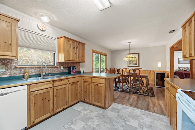 kitchen with kitchen peninsula, backsplash, white appliances, sink, and decorative light fixtures