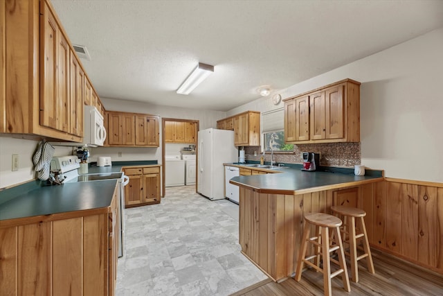 kitchen featuring sink, washing machine and dryer, kitchen peninsula, white appliances, and a breakfast bar