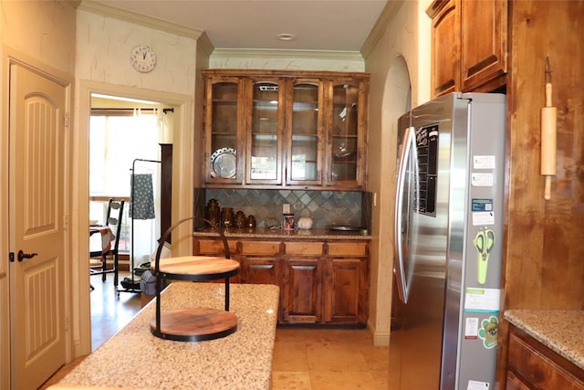 1104 Lynnwood Dr, Cleburne, TX 76033 - kitchen with freestanding refrigerator, ornamental molding, decorative backsplash, light stone counters, and brown cabinetry