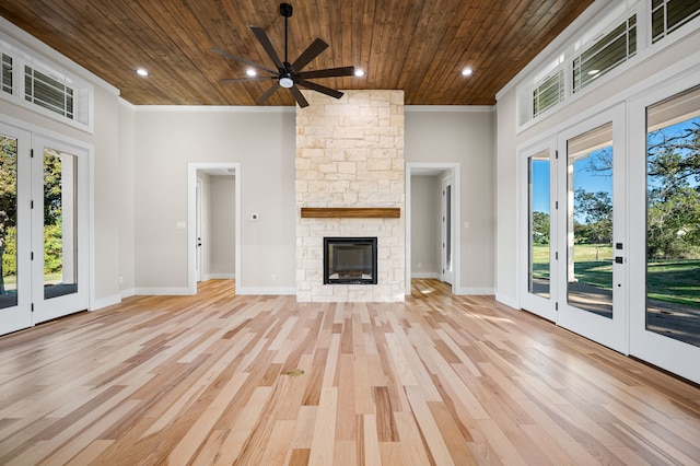 unfurnished living room featuring wood ceiling, light hardwood / wood-style flooring, ceiling fan, a stone fireplace, and french doors