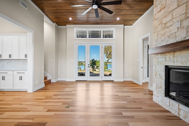 unfurnished living room with wood ceiling, a stone fireplace, light hardwood / wood-style flooring, and crown molding