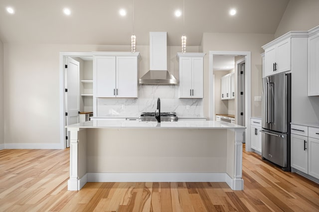 kitchen featuring a kitchen island with sink, high end fridge, wall chimney exhaust hood, and pendant lighting