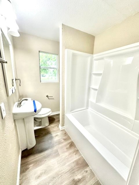 bathroom with shower / tub combination, a textured ceiling, hardwood / wood-style flooring, and toilet