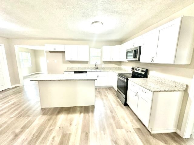 kitchen with light stone counters, stainless steel appliances, a center island, light hardwood / wood-style floors, and white cabinetry