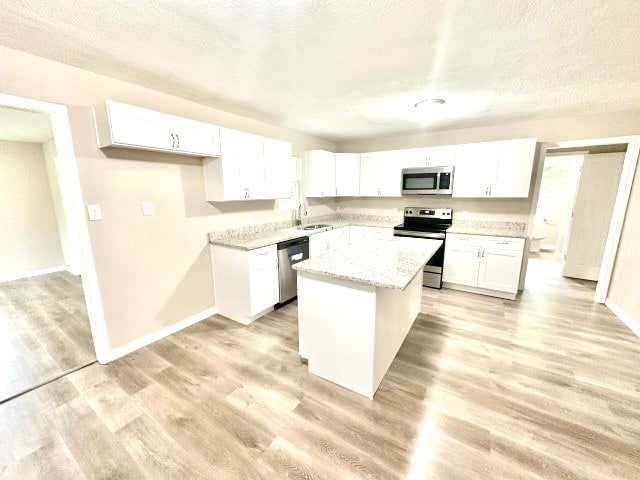 kitchen featuring sink, stainless steel appliances, a kitchen island, light hardwood / wood-style flooring, and white cabinets