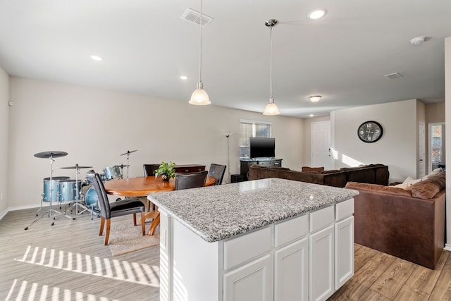 kitchen with pendant lighting, light wood-type flooring, a kitchen island, light stone counters, and white cabinetry