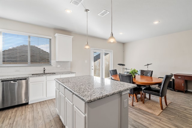 kitchen featuring a center island, hanging light fixtures, light hardwood / wood-style flooring, stainless steel dishwasher, and white cabinets