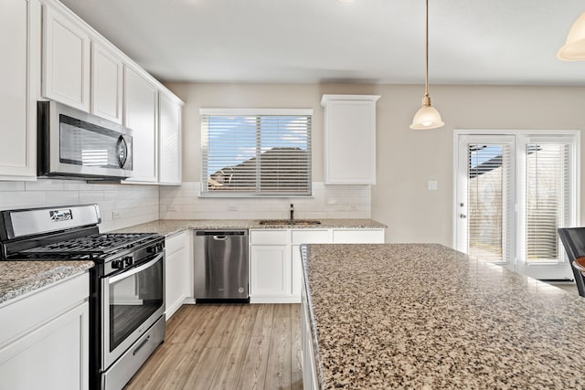 kitchen featuring appliances with stainless steel finishes, light stone counters, decorative light fixtures, light hardwood / wood-style floors, and white cabinetry