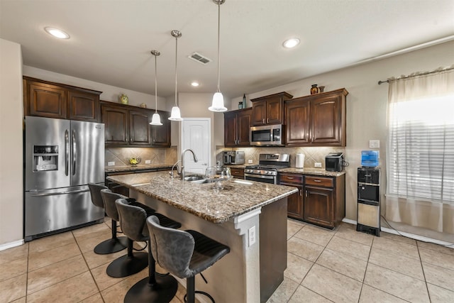 kitchen with pendant lighting, sink, an island with sink, appliances with stainless steel finishes, and dark brown cabinets