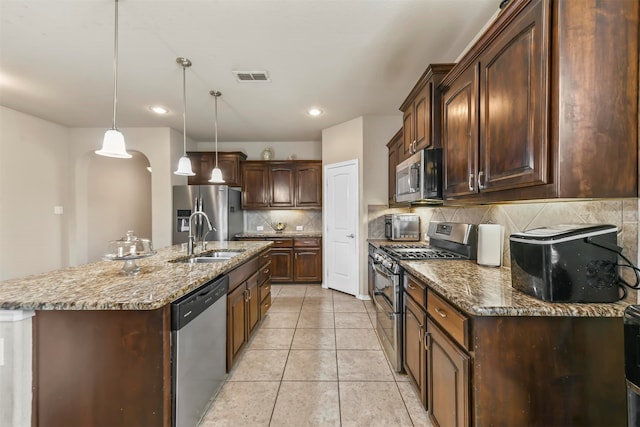 kitchen with a center island with sink, sink, tasteful backsplash, decorative light fixtures, and stainless steel appliances