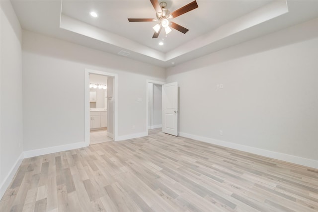 unfurnished bedroom featuring ensuite bath, a raised ceiling, ceiling fan, and light hardwood / wood-style floors