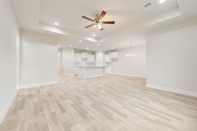 unfurnished living room featuring a raised ceiling, light hardwood / wood-style floors, and ceiling fan with notable chandelier