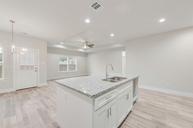 kitchen featuring white cabinets, ceiling fan with notable chandelier, a center island with sink, sink, and a tray ceiling