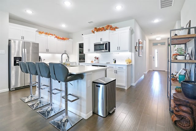 kitchen featuring appliances with stainless steel finishes, dark wood-type flooring, sink, a center island with sink, and white cabinetry